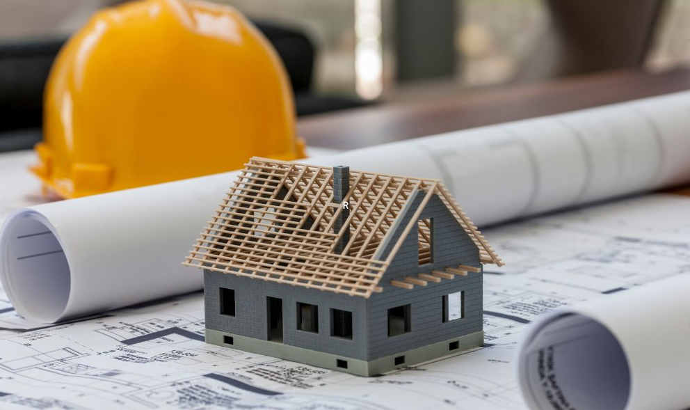 On aperçoit la maquette d'une maison posé sur une table entouré de plan de construction